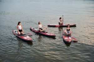 Young women paddling on stand-up paddleboards in a calm lake surrounded by nature.