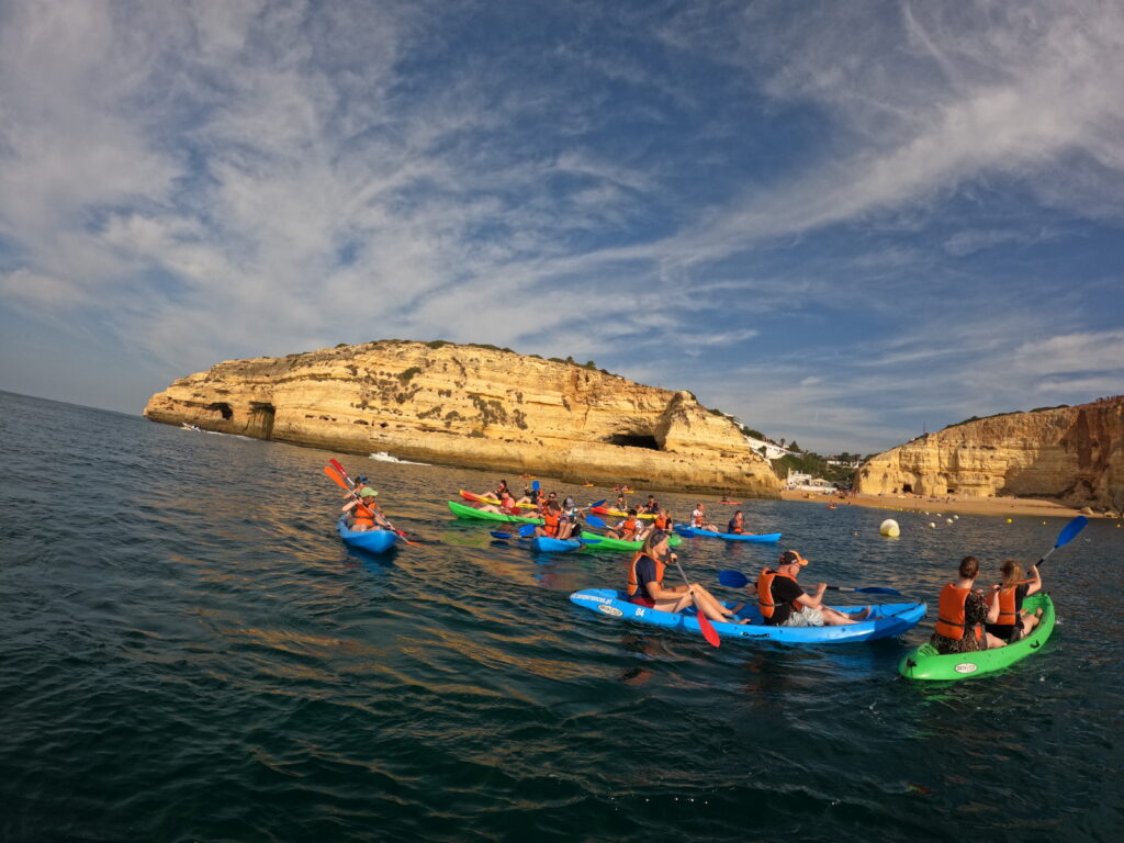 A group of kayakers paddling through the calm waters near the cliffs of Benagil Beach in the Algarve, Portugal.